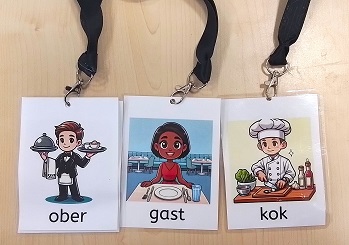 Drie rollenkaarten met afbeeldingen en tekst van de rollen "ober", "gast" en "restaurant", gelamineerd en bevestigd aan een keychord